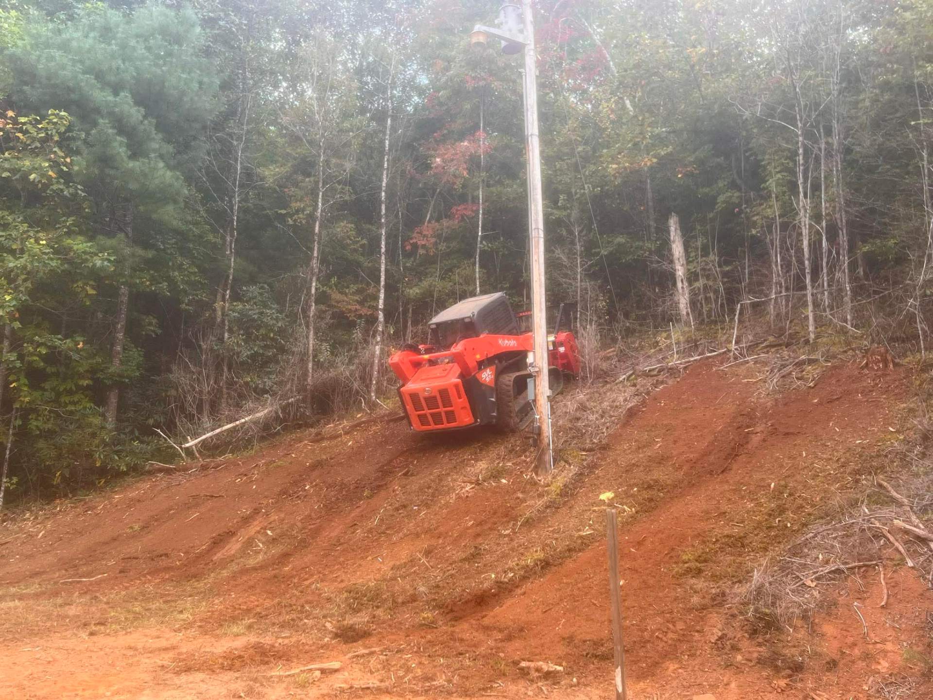 Kubota skid steer with mulcher climbing steep red clay hillside clearing brush in Florida