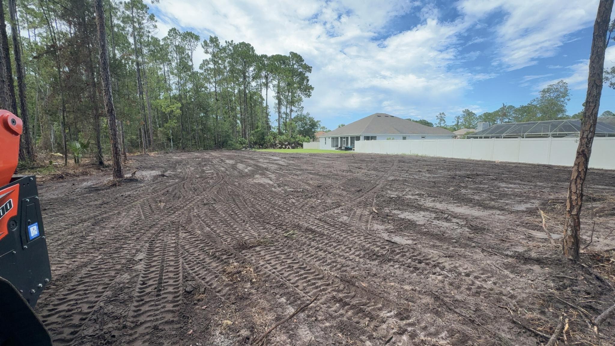 Kubota skid steer on freshly cleared residential lot next to homes with white fence in Deltona